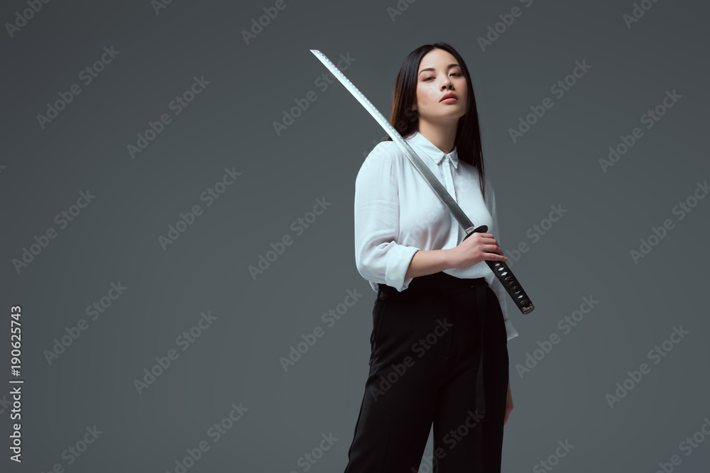 attractive young asian woman holding katana sword and looking at camera  isolated on grey foto de Stock | Adobe Stock