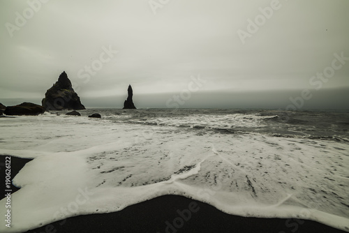 A beach with completely black sand and rocks sticking out of the water. Beach Vic. Iceland. Long exposure.
