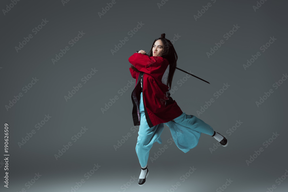 asian woman in kimono fighting with katana in jump on grey asian woman in kimono fighting with katana in jump on grey