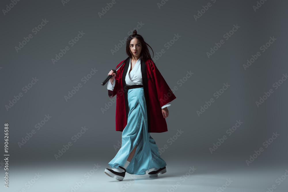 samurai in kimono walking with katana and looking at camera on grey