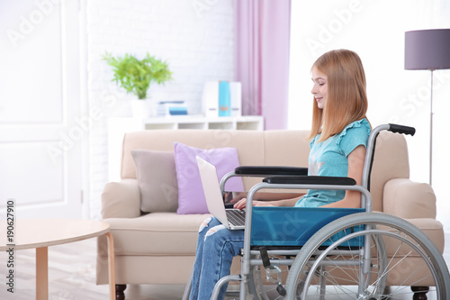 Teenage girl in wheelchair using laptop indoors