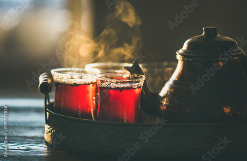 Traditional hot steaming Turkish tea in tulip glasses with copper pot in vintage tray