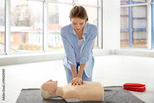 Young woman practicing first aid on mannequin indoors photo
