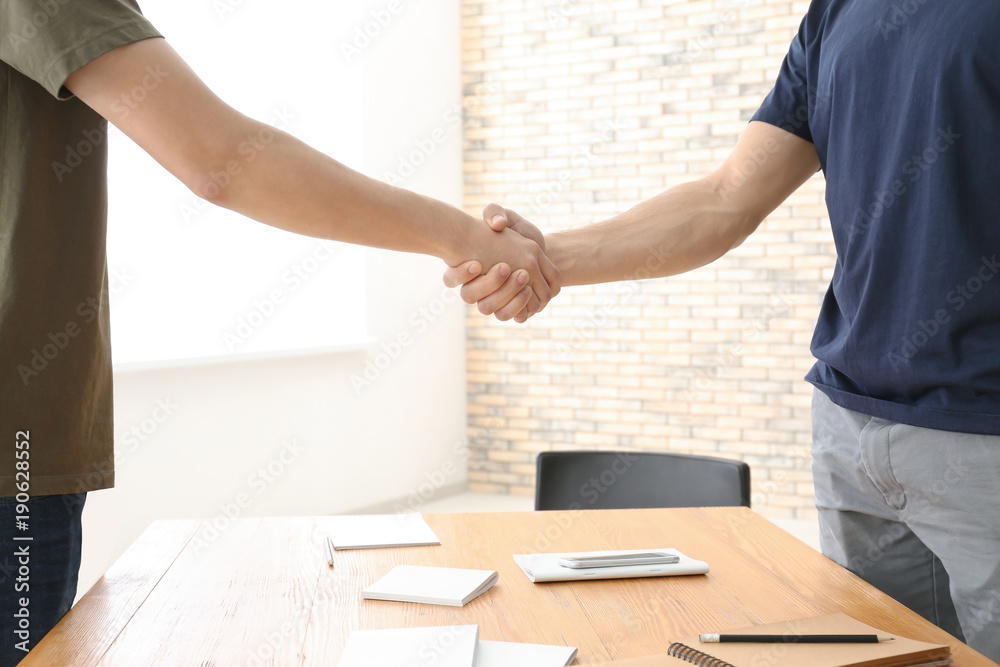 Obraz premium Two young men shaking hands over table. Unity concept