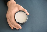 Male hand holding jar with clay for hair on grey background