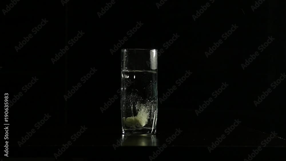 Close-up effervescent tablet dissolves in a glass of water on a dark background, slow motion Close-up effervescent tablet dissolves in a glass of water on a dark background, slow motion