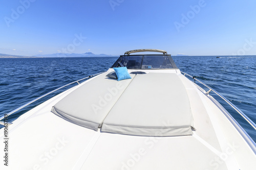 Luxury motorboat stern deck with white sunbeds, teak floor and coastal city view