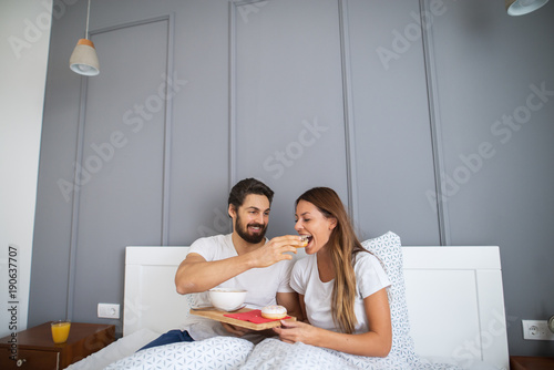 Bearded cheerful man giving beautiful young girl a bit of a breakfast in bed.