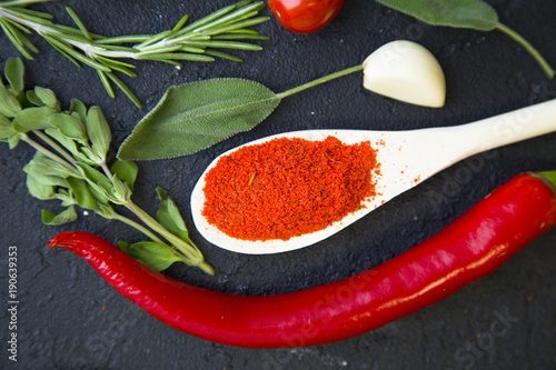 Cooking a hot spicy meal with a set of spices and herbs in wooden spoons, fresh rosemary, lettuce, garlc, and cayenne chili pepper, black concrete background, top view photo