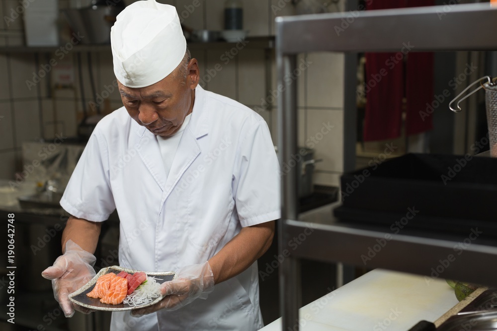 Senior chef holding plate of sushi in the kitchen Senior chef holding plate of sushi in the kitchen