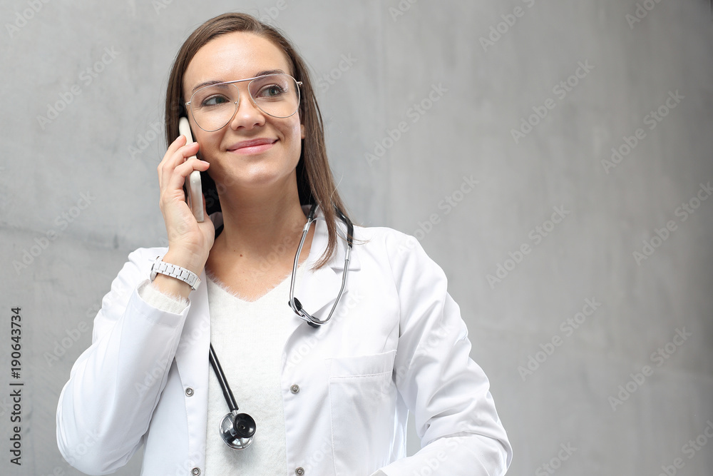 Młoda lekarka w białym kitlu rozmawia przez telefon - obrazy, fototapety, plakaty 