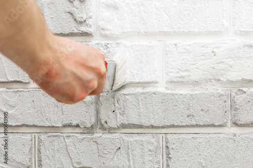 Male's hand painted with brush white brick wall.