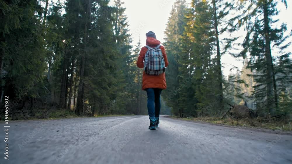 Nice Girl with Backpack is Walking on Beautiful Road Way in the Forest in Autumn. Beautiful Background Bottom View Nice Girl with Backpack is Walking on Beautiful Road Way in the Forest in Autumn. Beautiful Background Bottom View