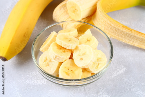 Bananas are whole and cut on a slice in a cup on a gray background.