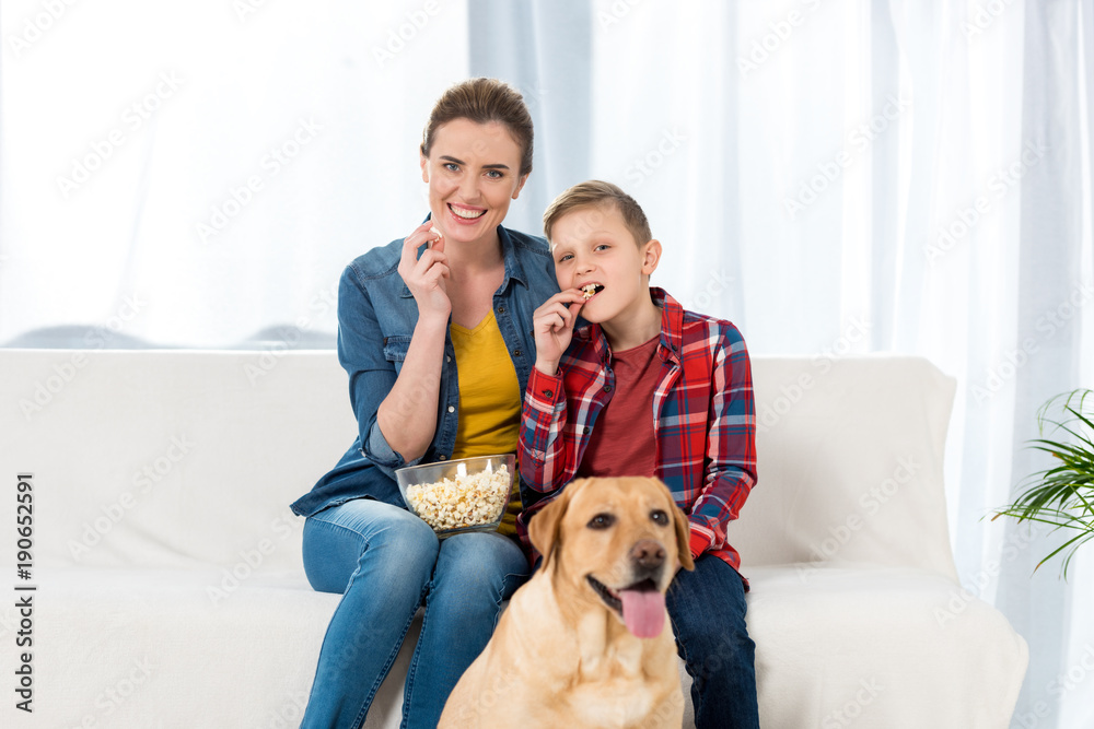 mother and son watching movie with popcorn while their dog sitting on floor mother and son watching movie with popcorn while their dog sitting on floor