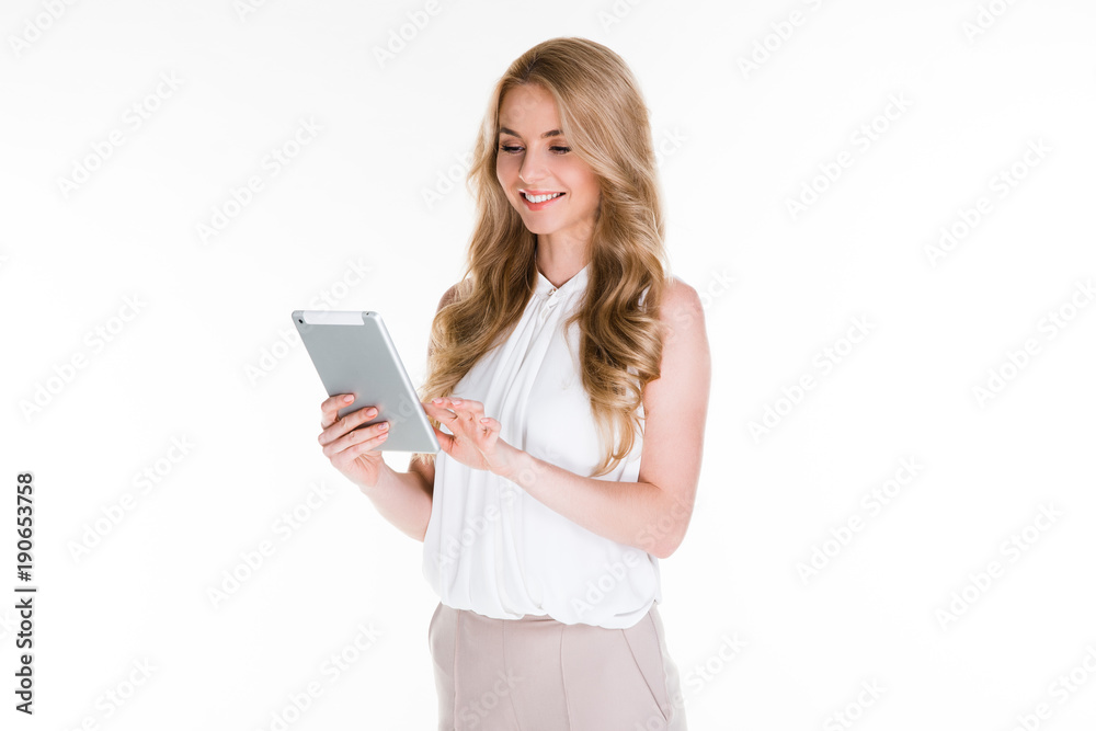 In one click. Beautiful young woman using her digital tablet and looking at it with smile while standing against white background In one click. Beautiful young woman using her digital tablet and looking at it with smile while standing against white background