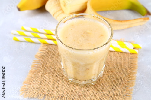 Banana smoothie with a paper tube and mint. Bananas are whole and cut on a gray background.