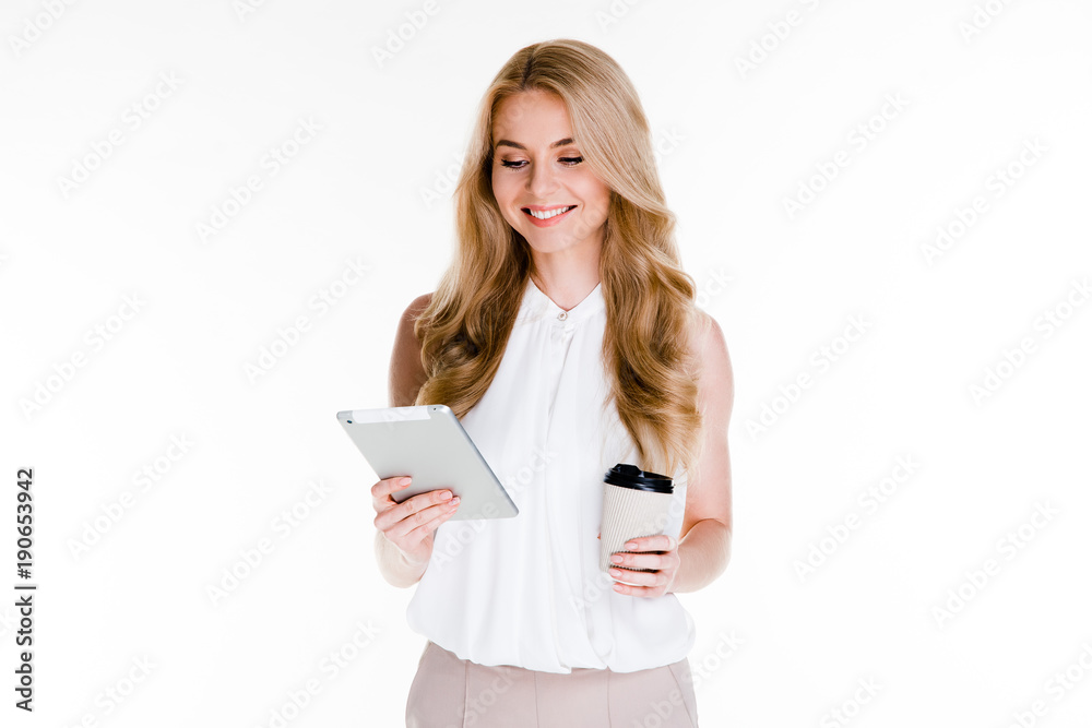 Spending great coffee break. Beautiful young woman using her digital tablet and looking at it with smile while standing against white background Spending great coffee break. Beautiful young woman using her digital tablet and looking at it with smile while standing against white background