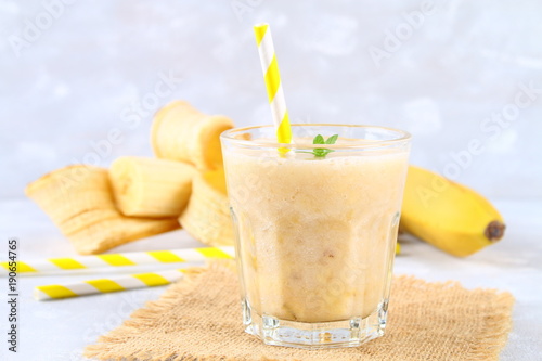 Banana smoothie with a paper tube and mint. Bananas are whole and cut on a gray background.