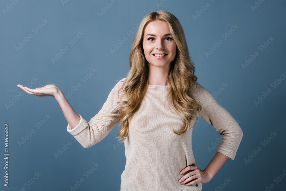 You product in her hands. Beautiful young woman looking at camera with smile and keeping arm outstretched while standing against black backgroun You product in her hands. Beautiful young woman looking at camera with smile and keeping arm outstretched while standing against black backgroun