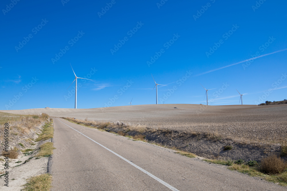 rural road next to wind power turbines on winter meadow near to Ampudia town, in Palencia Spain
