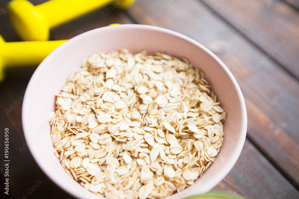 Healthy Breakfast, Sport, Fitness, Weight Loss, Diet Concept. Keeping fit with bowl of oatmeal and dumbbells, dark wooden background Healthy Breakfast, Sport, Fitness, Weight Loss, Diet Concept. Keeping fit with bowl of oatmeal and dumbbells, dark wooden background