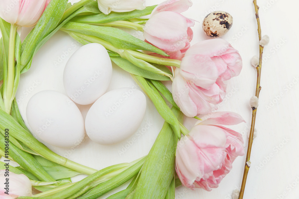 Spring greeting card. Easter eggs in the nest of tulips on white wooden background. Easter concept. Flat lay. Spring flowers tulips