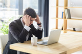 Young businessman suffers from headache while working on laptop