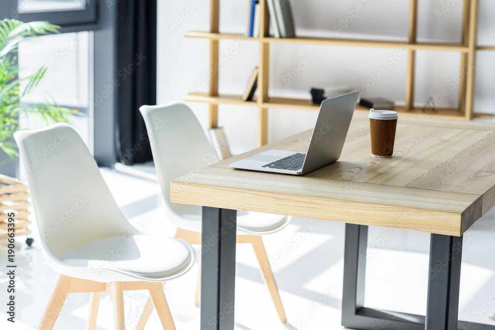 Laptop and coffe cup on table in modern office