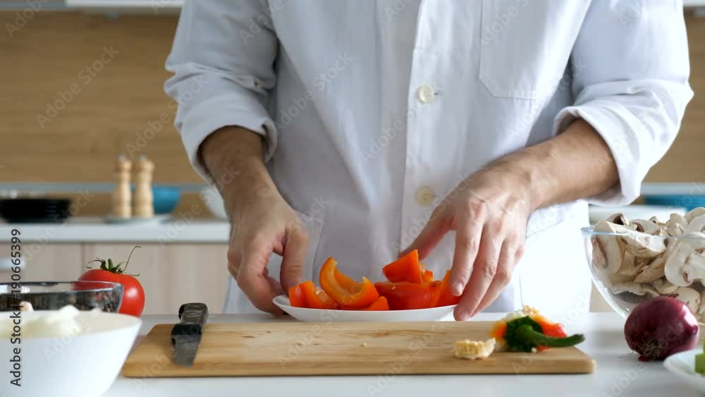 Male cook comes from the back of the kitchen and placing sweet red papper in a plate