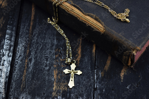 a golden cross lies and an ancient holy bible on the table