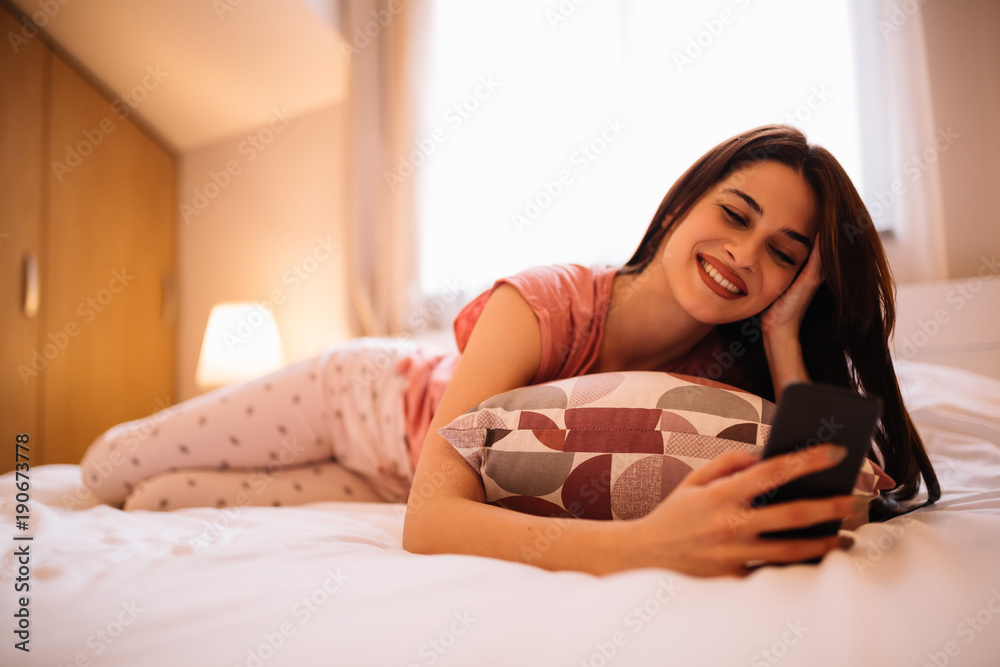 Young attractive girl lying on bed and using mobile
