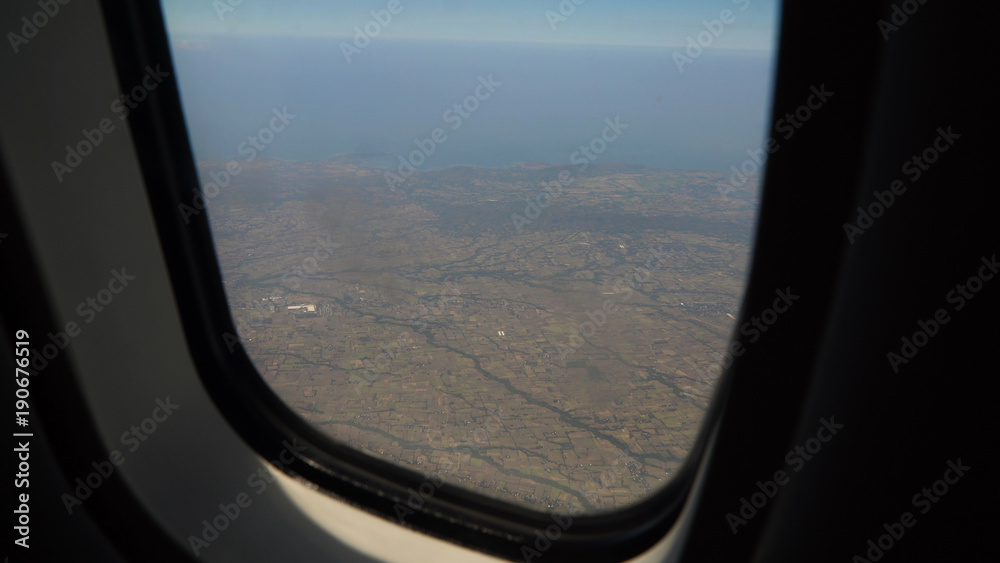 View through an airplane window on the tropical island, ocean, sky and clouds. Aerial view sea, clouds and sky as seen through window of an aircraft. Travel concept.