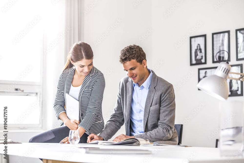 Happy young business people discussing over brochure at desk in office Happy young business people discussing over brochure at desk in office