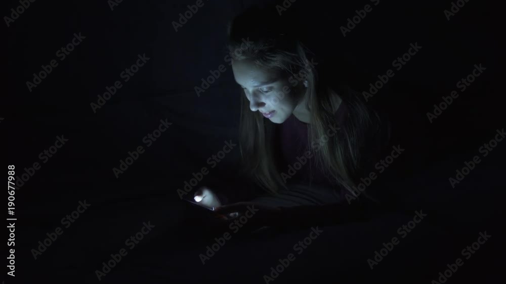 Girl sending message via cellphone in bed at night Girl sending message via cellphone in bed at night