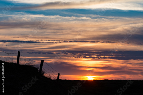 Sonnenuntergang auf Sylt, im Vordergrund die Silhouette eines Weidezauns