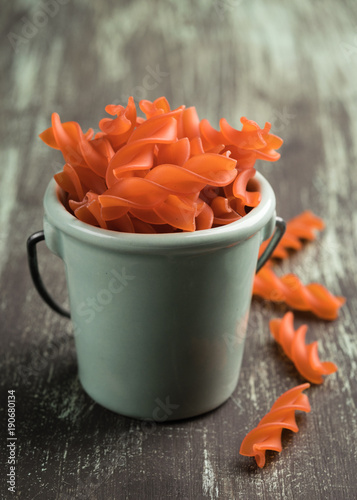 Closeup of a bowl full of uncooked red lentil fusilli on a rustic wooden table photo