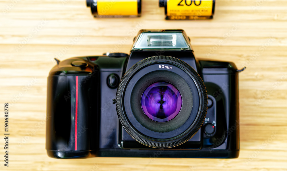 Analoge schwarze Spiegelreflexkamera auf einem Bambustisch mit zwei analogen Filmen im Hintergrund