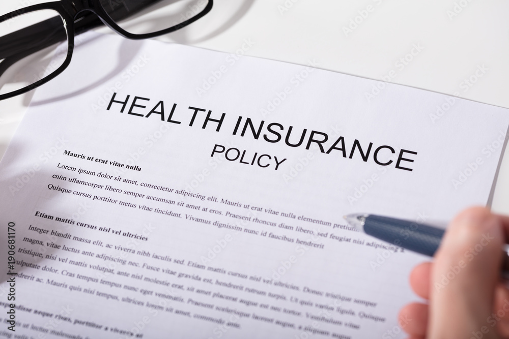 Person Holding Pen Over Health Insurance Policy Form Person Holding Pen Over Health Insurance Policy Form