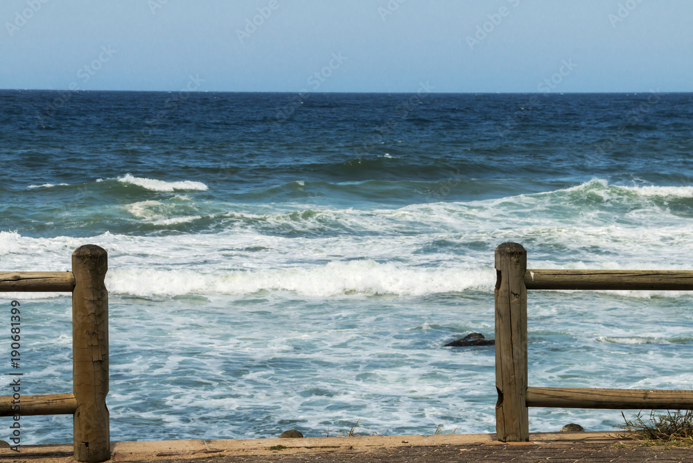 Wood Pole Barrier Sea Waves and Blue Skyline Background Wood Pole Barrier Sea Waves and Blue Skyline Background