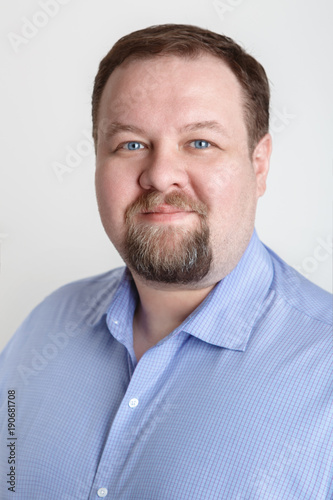 Close-up portrait of white Caucasian big fat stout business man with blue eyes looking directly in camera in studio on light background. Kind nice expression emotion