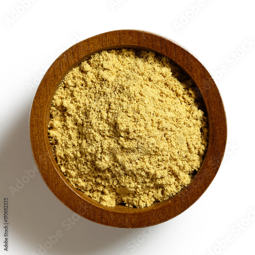 Finely ground dry ginger in dark wood bowl isolated on white from above.