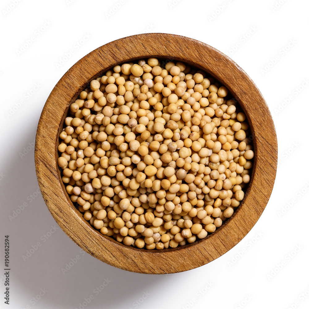 Dry white mustard seeds in dark wood bowl isolated on white from above. Dry white mustard seeds in dark wood bowl isolated on white from above.