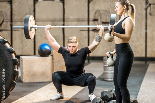 Young athletic couple in black sports wear training with weights in the crossfit gym