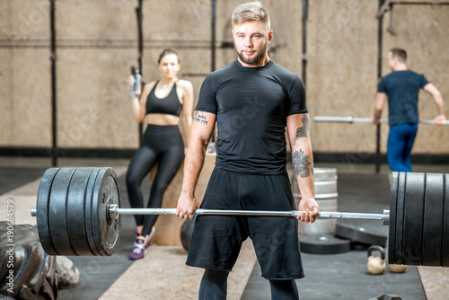 Handsome athletic man in black sports wear lifting up a heavy burbell in the crossfit gym