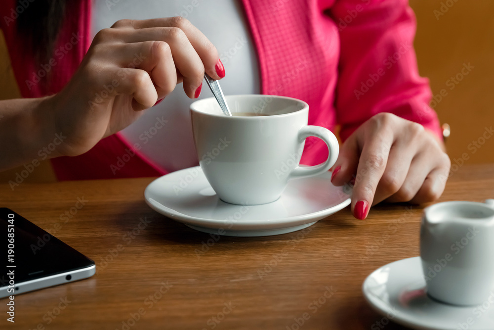 Close-up, hands of a young girl, stirs sugar in a cup of coffee, sits in a cafe behind a wooden stolikos. Business lunch, modern girl. Close-up, hands of a young girl, stirs sugar in a cup of coffee, sits in a cafe behind a wooden stolikos. Business lunch, modern girl.