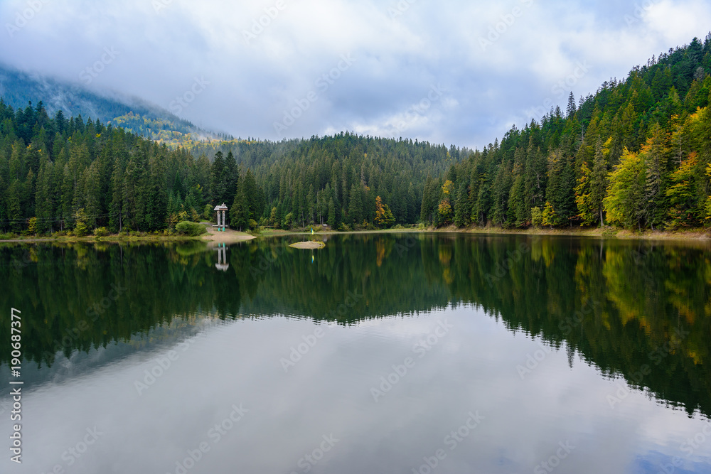 View of Synevir high-altitude lake by autumn day. The leaf fall forest is reflected in water of lake.