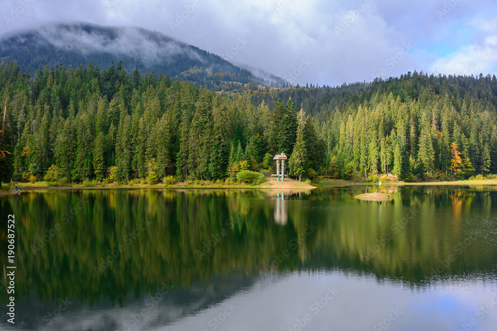 View of Synevir high-altitude lake by autumn day. The leaf fall forest is reflected in water of lake.