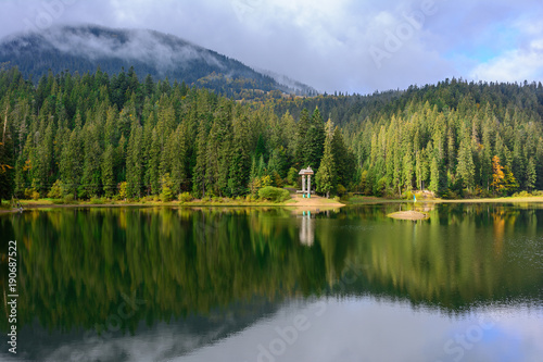 View of Synevir high-altitude lake by autumn day. The leaf fall forest is reflected in water of lake. © iryna_l