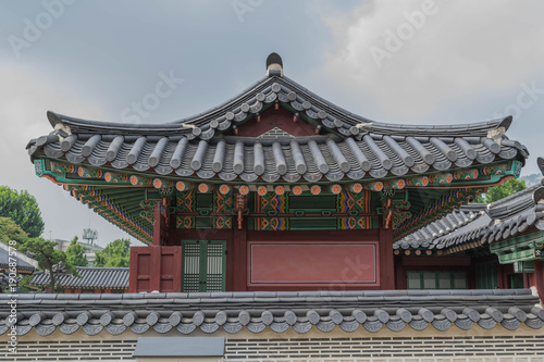 A fancy tiled rooftop, colorful architectural elements and a partial tile wall, at Gyeongbokgung Palace, in Seoul, South Korea